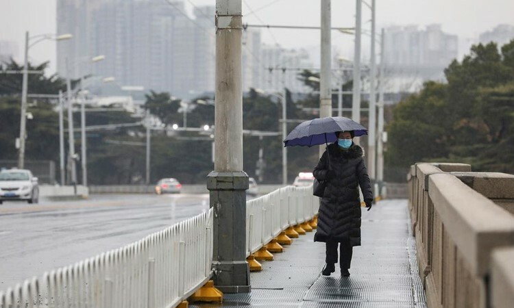 Người phụ nữ đeo khẩu trang đi bộ trên cầu dưới trời mua ở Vũ Hán, tỉnh Hồ Bắc hôm 25/1. Ảnh: AP.